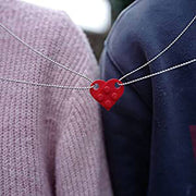 Close-up of a red heart-shaped acrylic necklace worn by a couple, symbolizing love and connection.